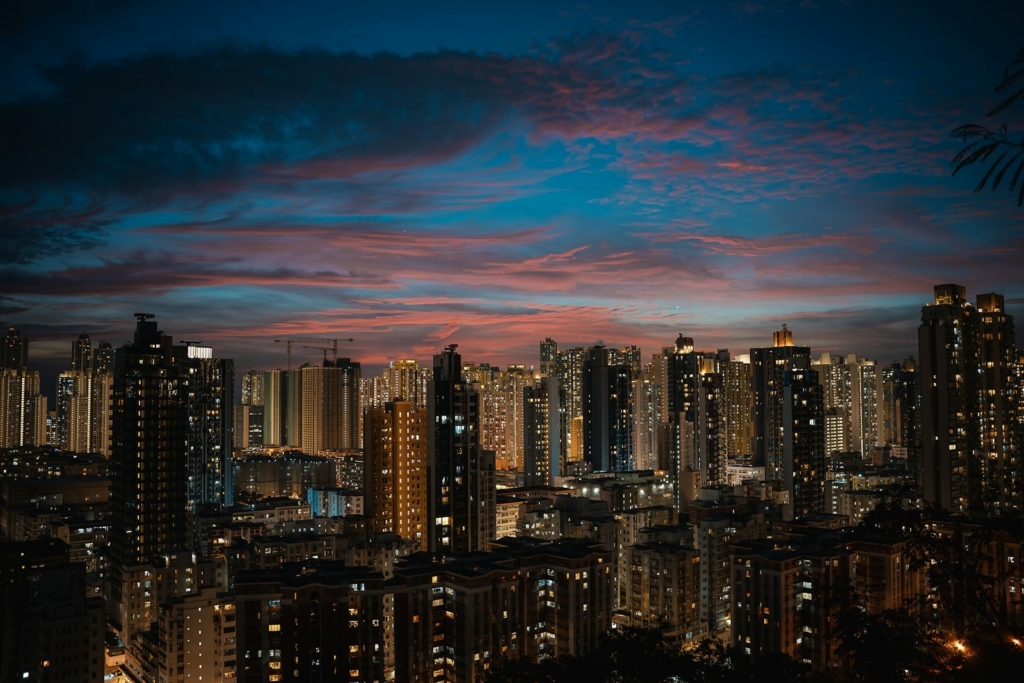 Cityscape at dusk with illuminated buildings and colorful sky.